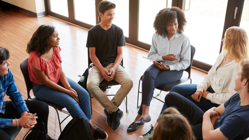 Group of people sat in a circle discussing wellbeing support at their team meeting